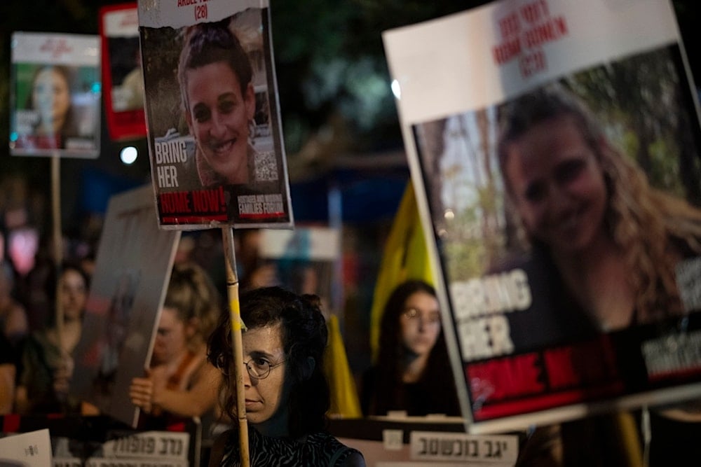 People hold portraits of the captives taken in Hamas’ October 7 attack, in occupied al-Quds, Tuesday, August 20, 2024 (AP)