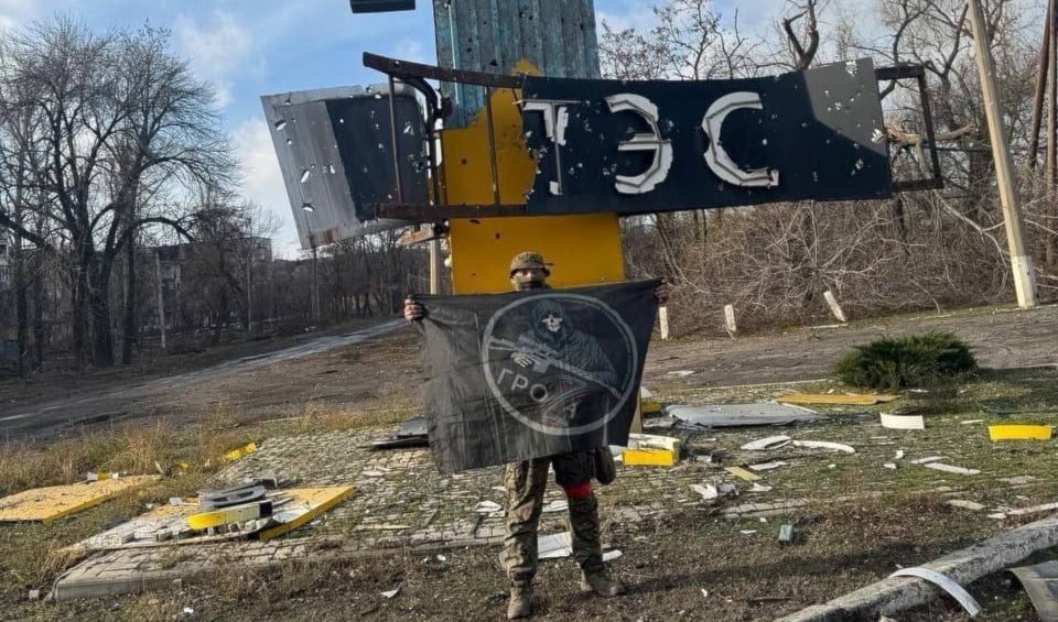 A Russian soldier is photographed holding a flag in front of a damaged tower. (Telegram)