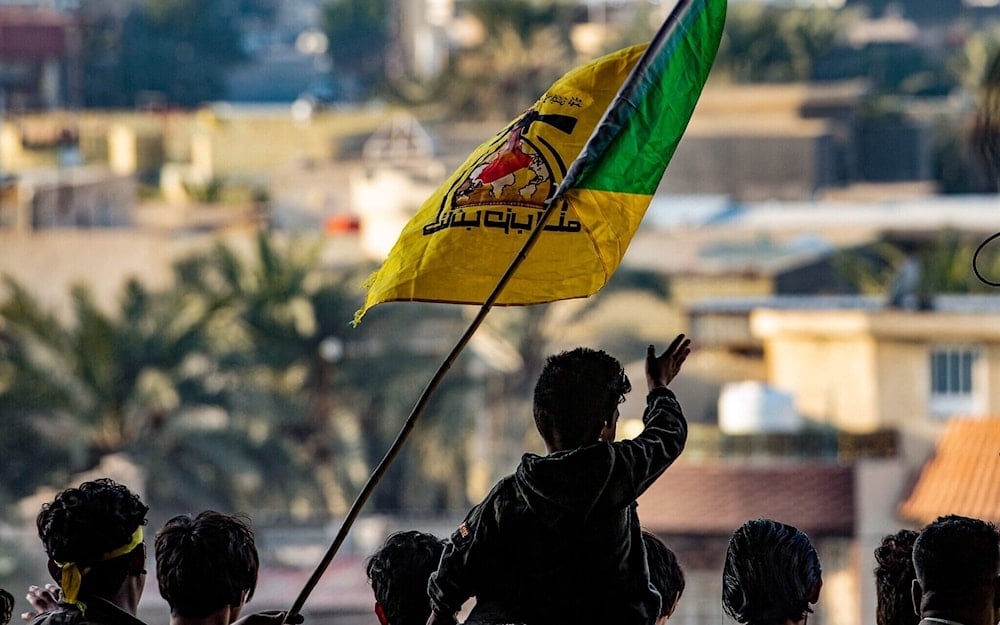 Young men raise the flag of Kataeb Hezbollah during a ceremony marking the second anniversary of the martyrdom of Major General Qassem Soleimani and Abu Mahdi al-Muhandis on January 8, 2022, Basra, Iraq (AFP)