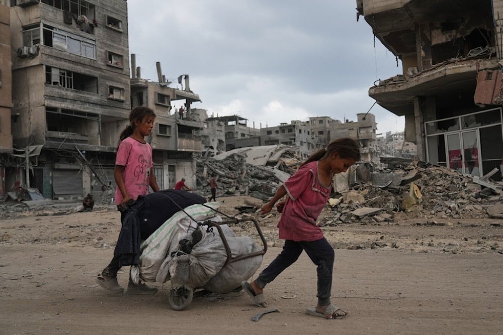 Two Palestinian girls pull a cart loaded with belongings as they walk along the heavily damaged al-Jalaa Street in Gaza City, Sunday, October 12, 2025 (AP)