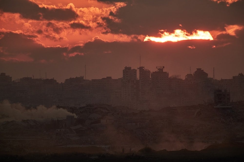 The sun sets behind buildings destroyed during the Israeli aggression in the northern Gaza Strip, as seen from southern occupied Palestine, Tuesday, October 14, 2025 (AP)