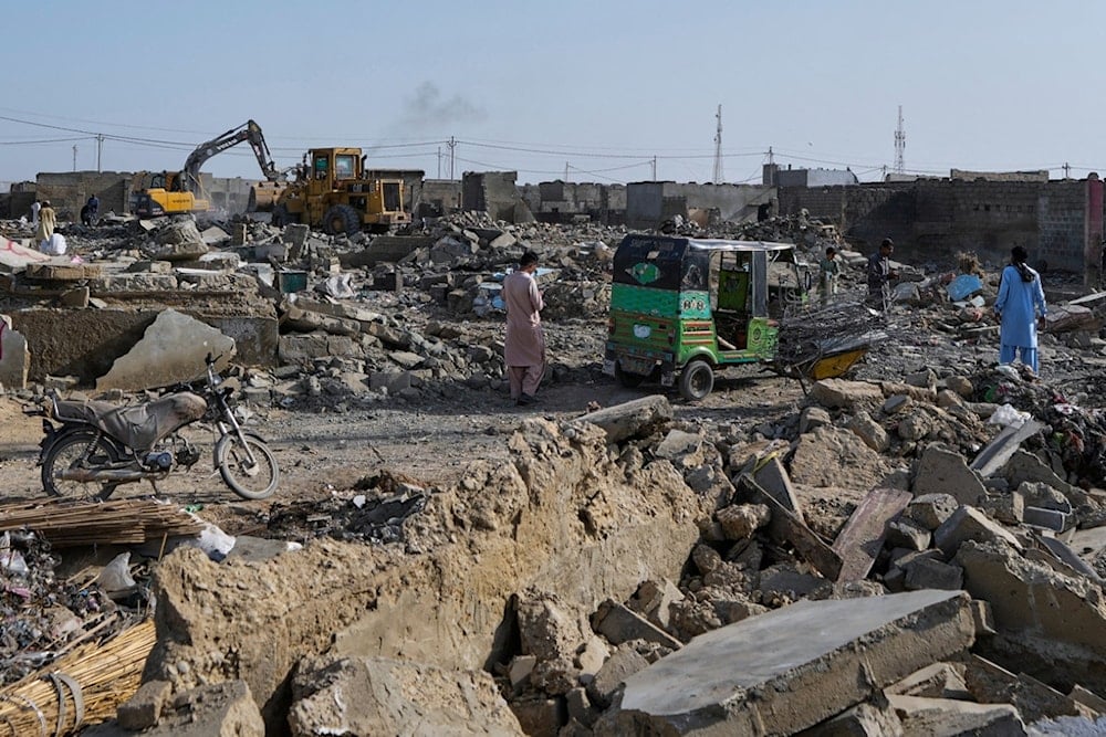 People walk through rubble as a hydraulic shovel demolishes a structure during an operation against illegal settlement of Afghan refugees conducted by local government, on the outskirts of Karachi, Pakistan, Wednesday, October 15, 2025 (AP)