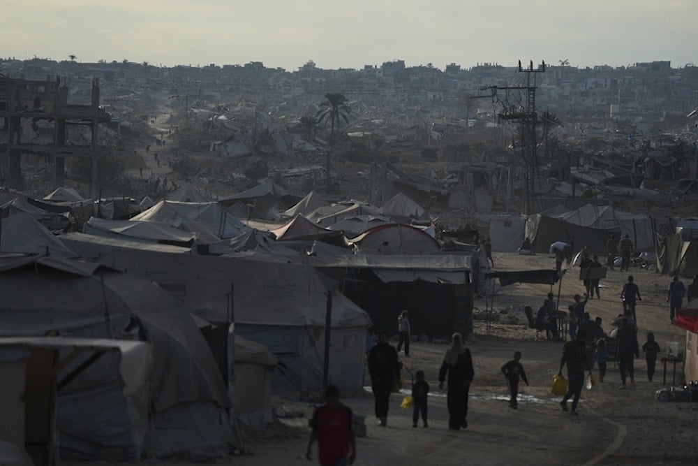 Displaced Palestinians walk trough a tent camp adjacent to destroyed homes and buildings in Khan Younis, Gaza Strip, Saturday, October 18, 2025 (AP)