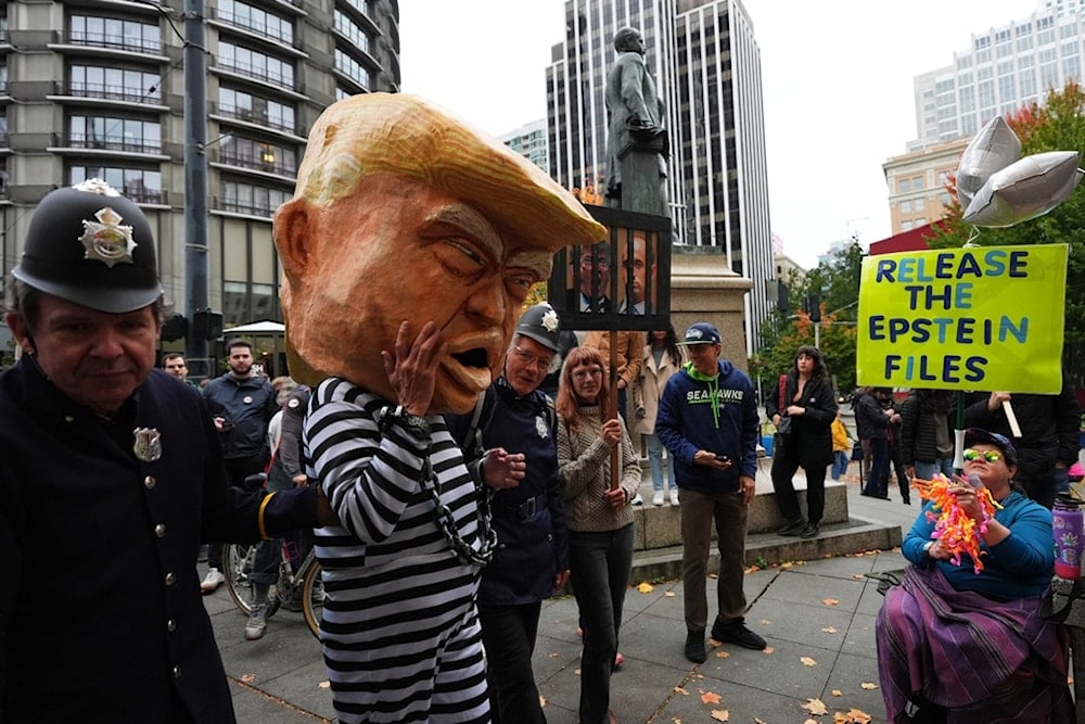 A protester dressed as US President Donald Trump in chains and a prison jumpsuit looks at another holding a sign referencing the Epstein files as people take part in a 