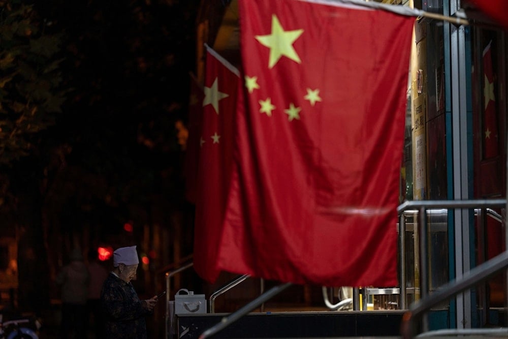An elderly woman stands near Chinese national flags hung for the national day holidays during the mid-autumn festival in Beijing, Monday, Oct. 6, 2025. (AP Photo/Ng Han Guan)