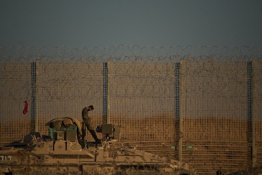 An Israeli soldier stands on top of an armored personnel carrier (APC) parked in an area at the border with the Gaza Strip, as seen from southern occupied Palestine, Tuesday, October 21, 2025 (AP)