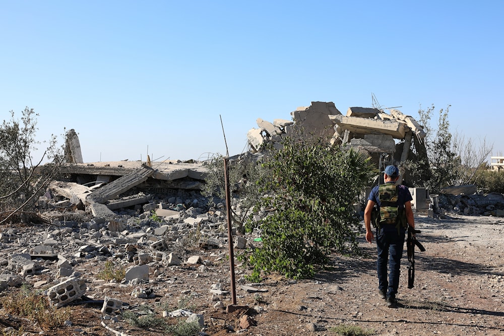 A gunman walks by the remains of a house destroyed during the recent sectarian clashes in the Druze-majority town of Sweida, southern Syria, on Sept. 19, 2025 (AP)
