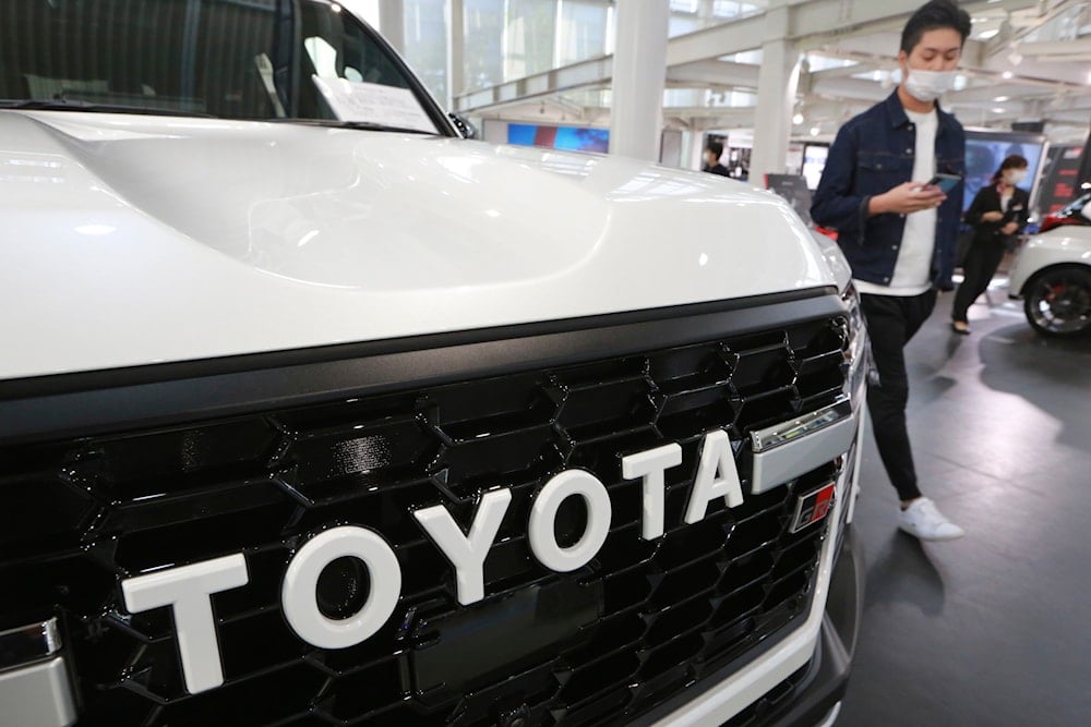 A man walks by the logo on a Toyota car at a showroom in Tokyo on Oct. 18, 2021. The shortage of parts caused by the coronavirus pandemic is further denting production at Toyota, Japan’s top automaker. (AP Photo/Koji Sasahara, File)