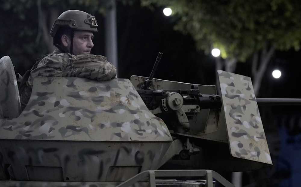 A Lebanese army soldier sits behind his weapon on the top of an armored personnel carrier at the site of an Israeli airstrike in Beirut's southern suburb on September 23, 2024. (AP)