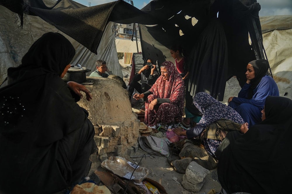 Palestinian women bake bread in a clay oven, using plastic for fire, at a UN school used as a shelter for displaced Palestinians in Khan Younis, Sunday, Oct. 5, 2025 (AP)