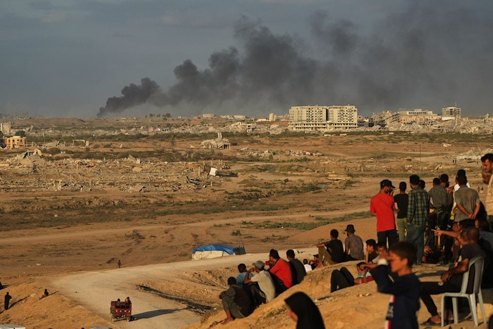 Displaced Palestinians watch smoke rise after Israeli military strikes as they gather on the coastal road near Wadi Gaza, in the central Gaza Strip, Thursday, October 9, 2025 (AP)