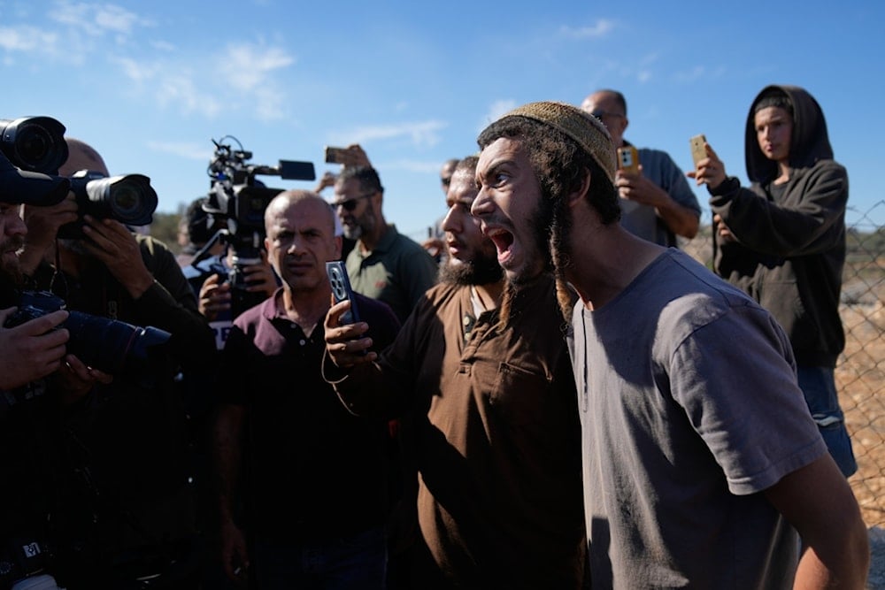 Israeli settlers take pictures of foreign activists and farmers while they attempt to disrupt the harvest of olive groves by Palestinian farmers, in the West Bank town of Silwad, Wednesday, October 29, 2025 (AP)