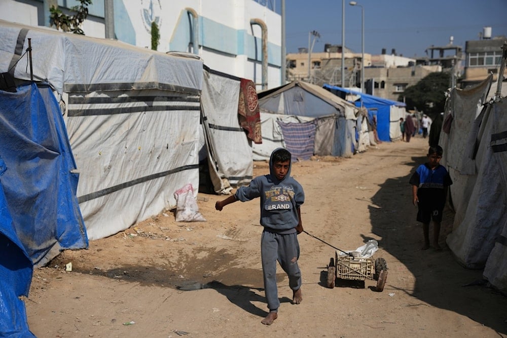 A Palestinian child pulls a cart between tents temporarily erected in a camp in Deir al‑Balah, central Gaza Strip, Saturday, November 1, 2025 (AP)