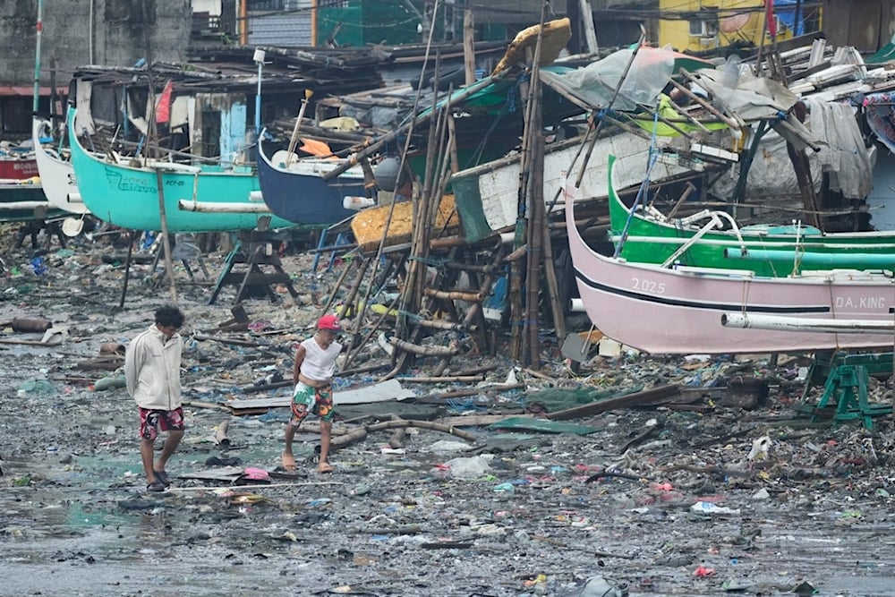 Residents walk on debris that was washed ashore due to Typhoon Fung-wong along a coastal village on Monday, Nov. 10, 2025, in Navotas, Philippines. (AP Photo/Aaron Favila)