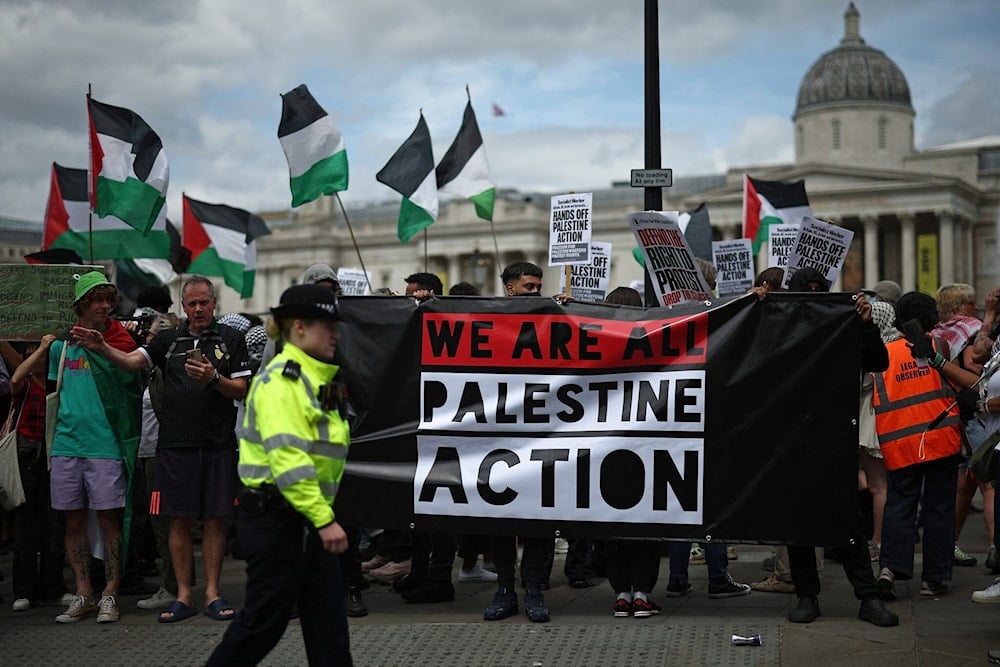 Police officers monitor protesters holding a banner during a protest in support of anti-Israel, pro-Palestinian group Palestine Action, in Trafalgar Square, central London, on June 23, 2025. (Henry Nicholls / AFP)