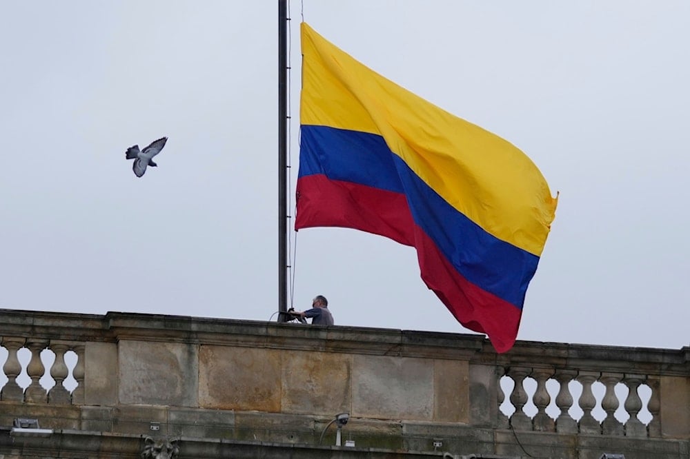 A worker raises the flag at Congress in Bogota, Colombia, Monday, Aug. 11, 2025. (AP Photo/Fernando Vergara)