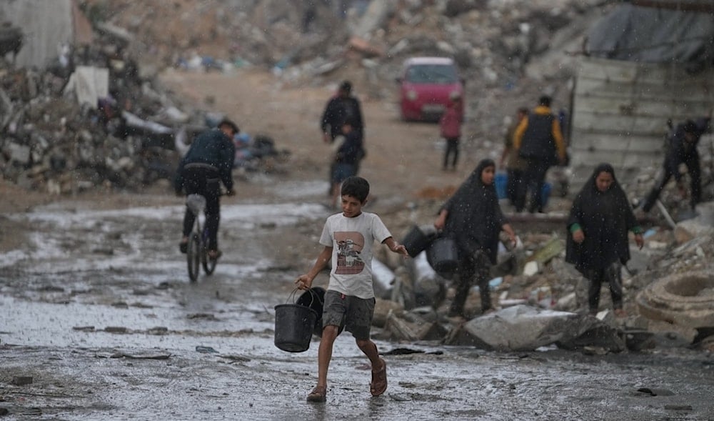 A boy carries two empty buckets on his way to collect water amid a rainstorm in the Sheikh Radwan neighborhood of Gaza City, Friday, Nov. 14, 2025. (AP)