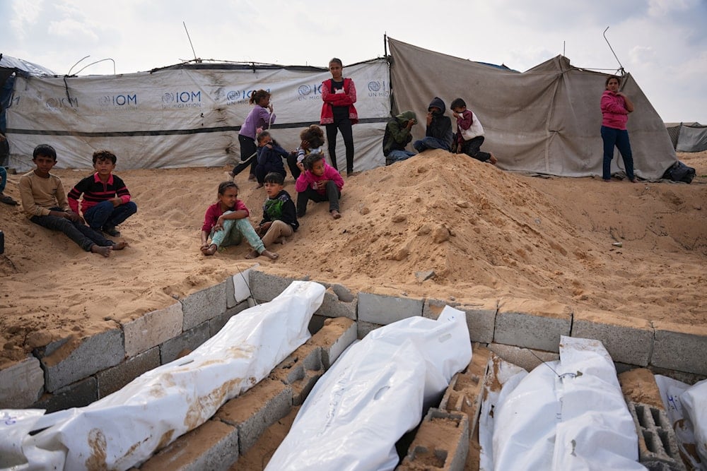 Children watch as bodies of unidentified Palestinians returned from Israel as part of the ceasefire deal are buried in Deir al-Balah, Gaza Strip, Friday, Nov. 14, 2025 (AP)