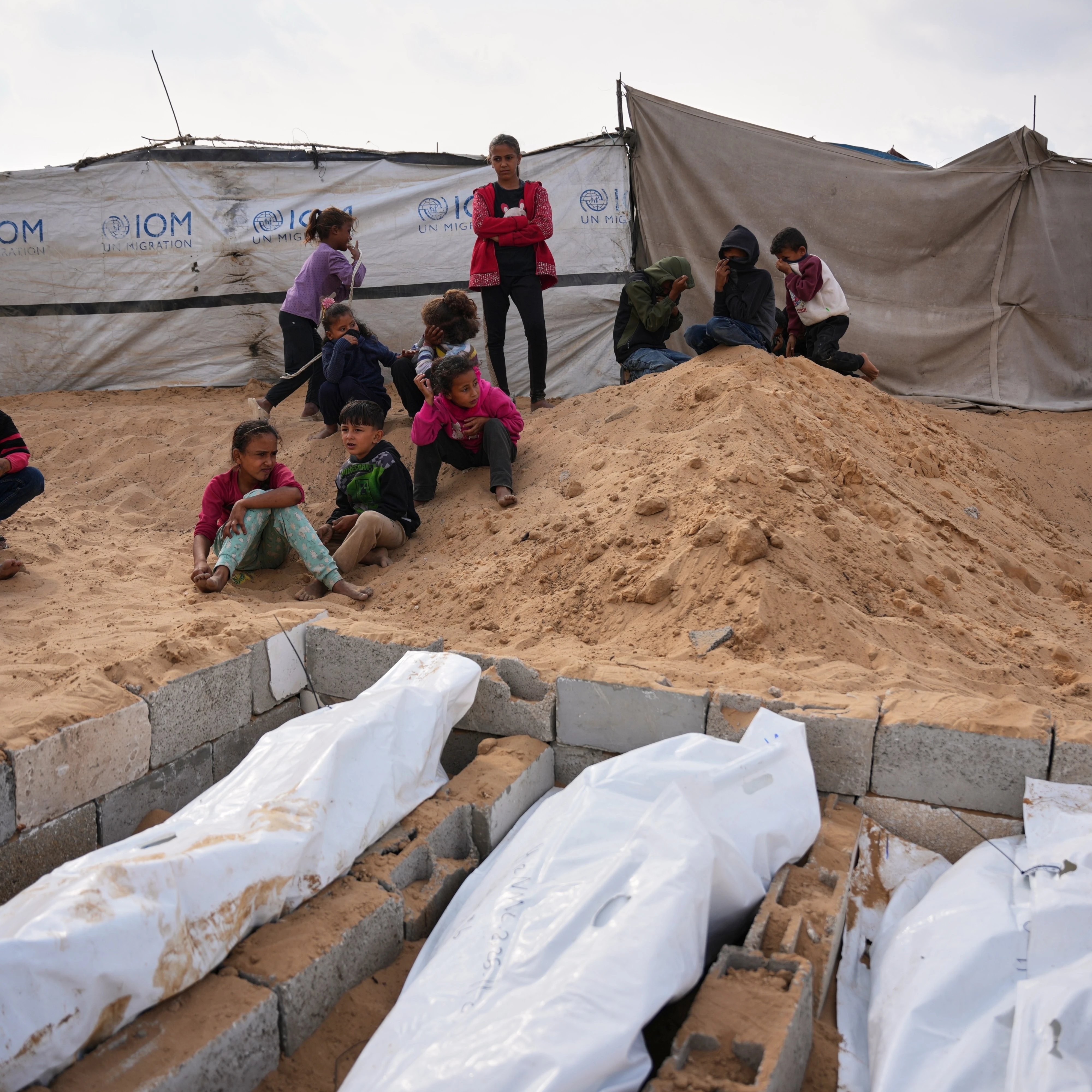 Children watch as bodies of unidentified Palestinians returned from Israel as part of the ceasefire deal are buried in Deir al-Balah, Gaza Strip, Friday, Nov. 14, 2025 (AP)