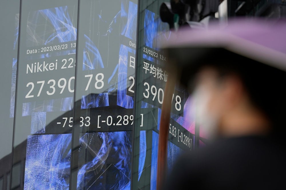 A person stands in front of an electronic stock board showing Japan's Nikkei 225 index at a securities firm in the rain on March 23, 2023, in Tokyo. (AP)