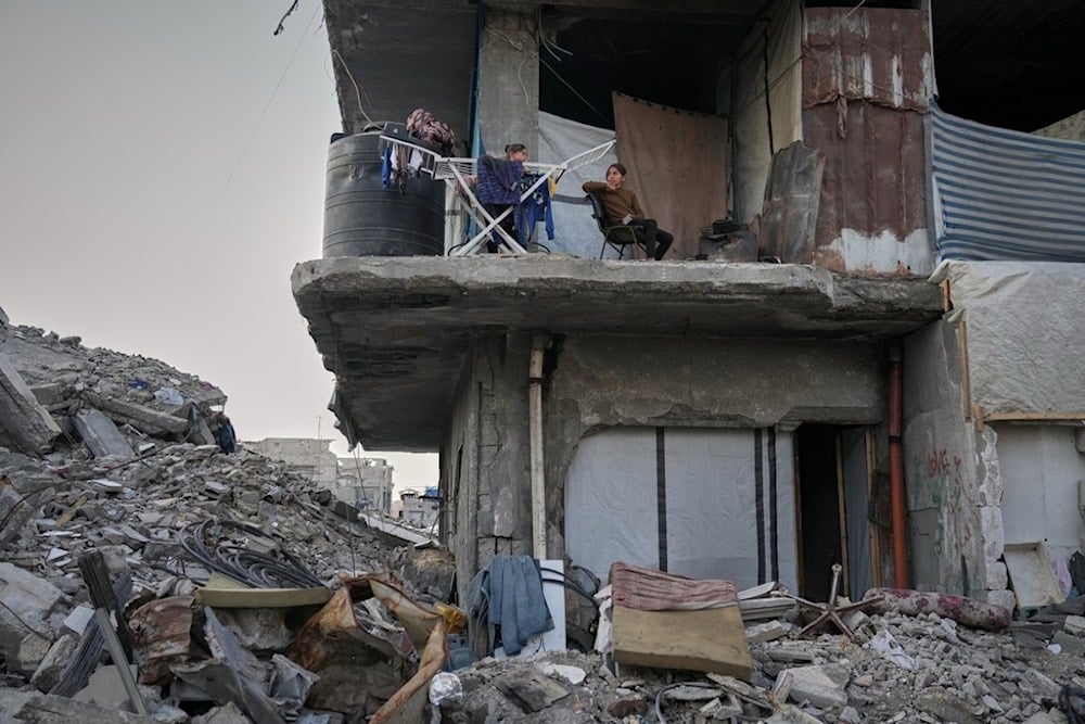 Two girls sit next to their drying laundry in a gutted apartment building in Gaza City, Tuesday, November 18, 2025 (AP)