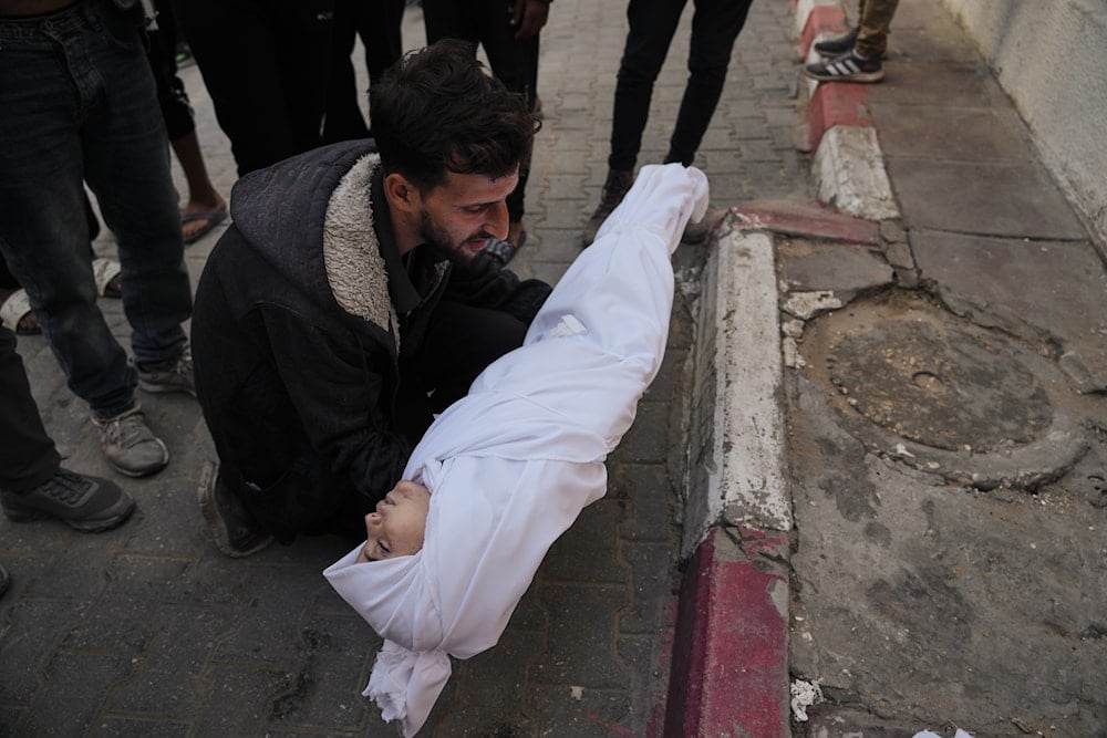 A man carries the body of a child from the Azzam family, killed in Israeli strikes, during her funeral at Shifa Hospital in Gaza City Thursday, Nov. 20, 2025 (AP)
