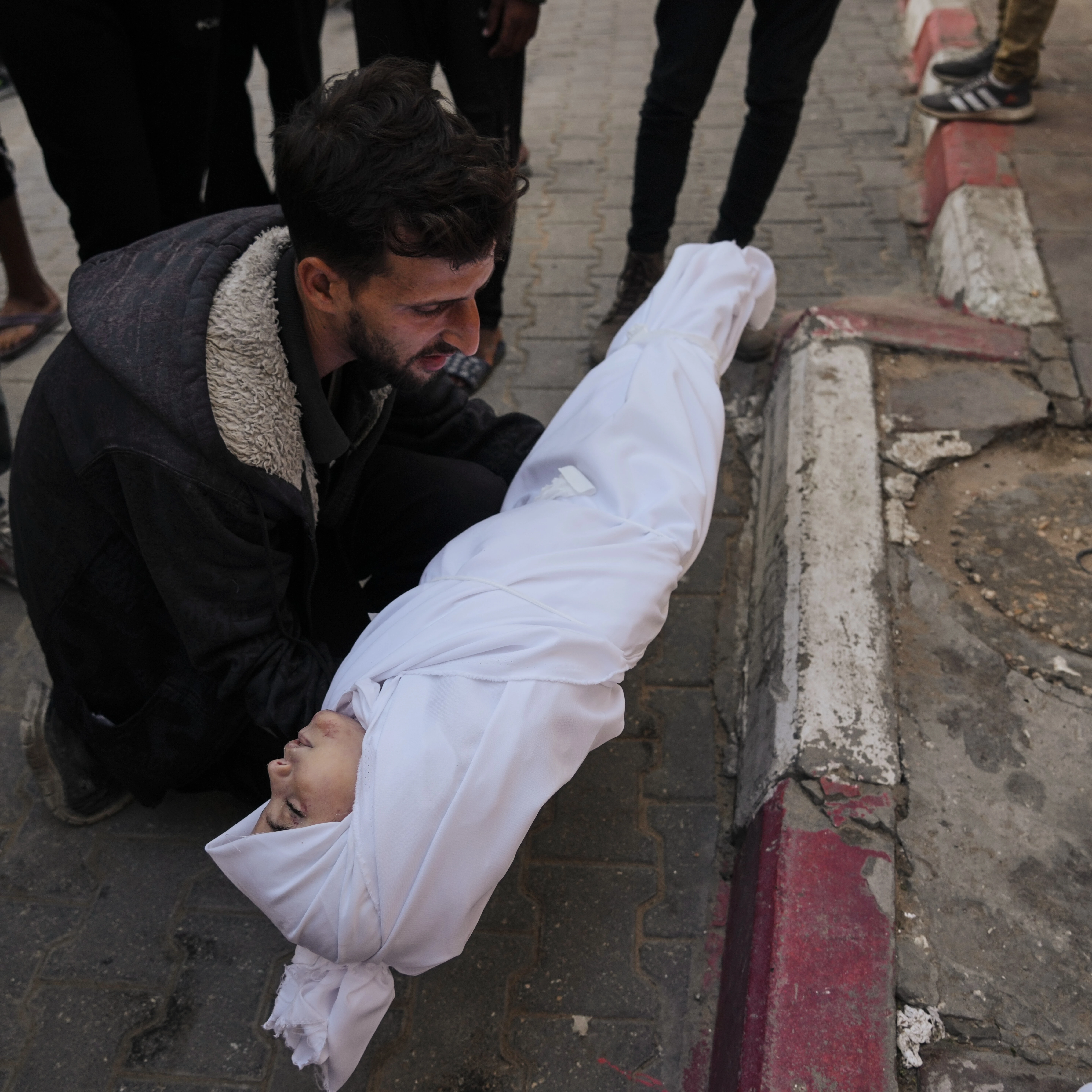 A man carries the body of a child from the Azzam family, killed in Israeli strikes, during her funeral at Shifa Hospital in Gaza City Thursday, Nov. 20, 2025 (AP)