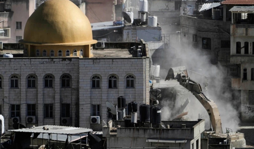 An Israeli army bulldozer demolishes homes next to a mosque in the Palestinian urban refugee camp of Nur Shams, in the West Bank, Tuesday, May 6, 2025. (AP Photo/Majdi Mohammed)