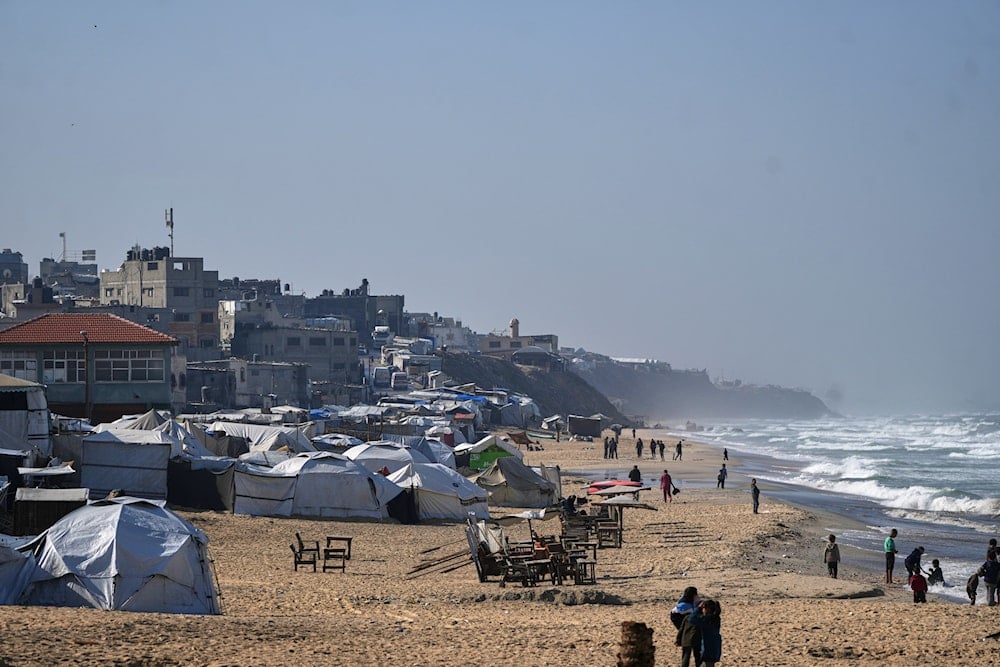 Palestinians walk along the beachfront next to a temporary tent camp in Deir al-Balah, in the central Gaza Strip, Saturday, Nov. 15, 2025 (AP)