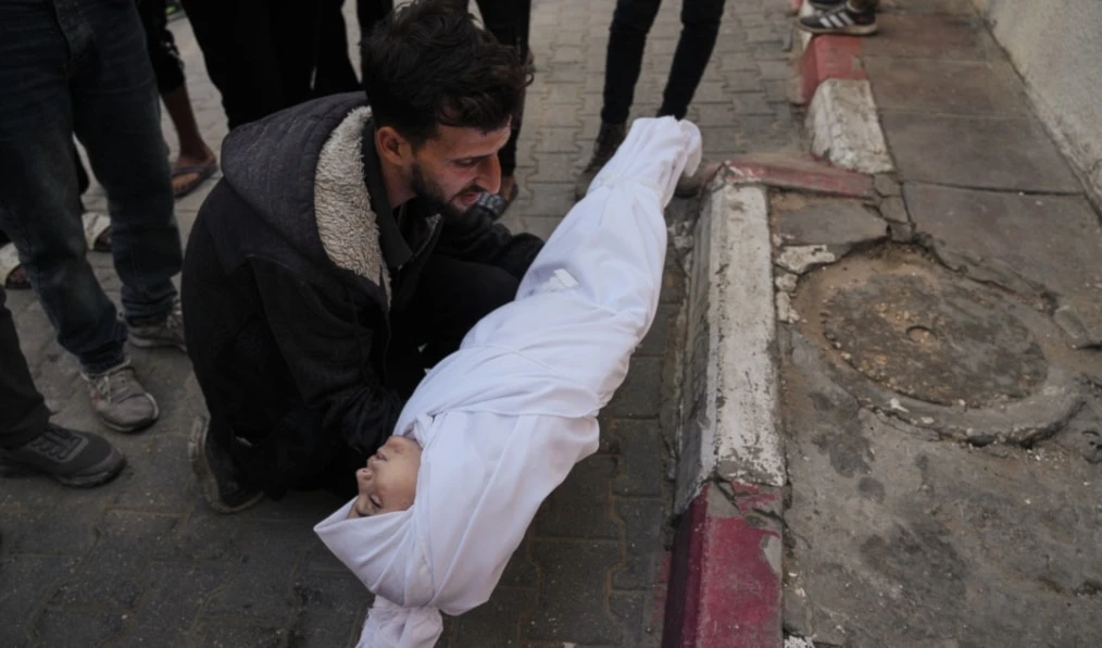 A man carries the body of a child from the Azzam family, killed in Israeli strikes, during her funeral at Shifa Hospital in Gaza City, Nov. 20, 2025. (AP)