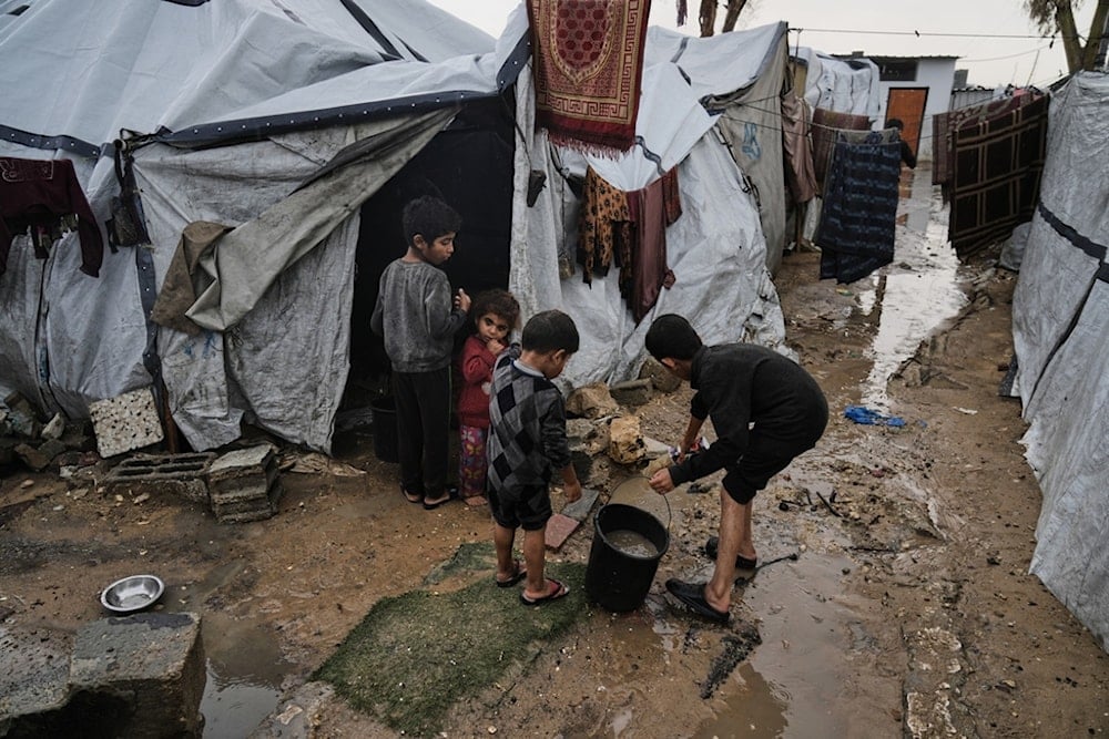 Displaced Palestinian children clear water from their flooded tent at a temporary camp after heavy rainfall in Gaza City, Tuesday, November 25, 2025 (AP)