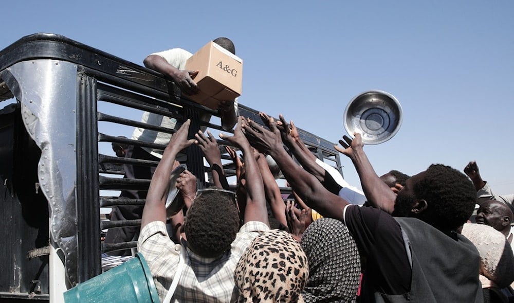 Sudanese families displaced from El-Fasher reach out as aid workers distribute food supplies at the newly established El-Afadh camp in Al Dabbah, in Sudan's Northern State, Nov. 16, 2025. (AP)