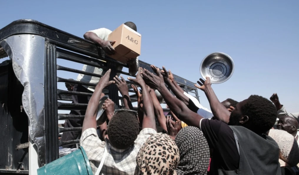 Sudanese families displaced from El-Fasher reach out as aid workers distribute food supplies at the newly established El-Afadh camp in Al Dabbah, in Sudan's Northern State, Nov. 16, 2025. (AP)