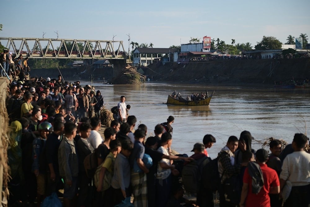People wait for a boat to ride across a river after a bridge nearby collapsed during a flood in Bireun, Aceh province, Indonesia, Saturday, November 29, 2025 (AP)