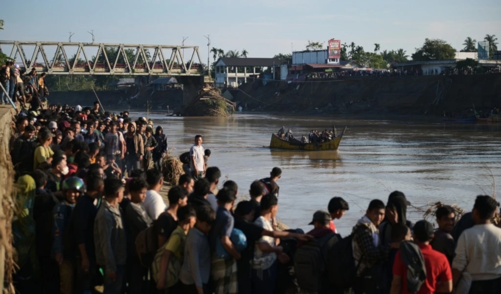 People wait for a boat to ride across a river after a bridge nearby collapsed during a flood in Bireun, Aceh province, Indonesia, Saturday, November 29, 2025 (AP)