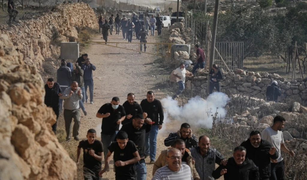 Palestinians and activists run away from tear gas shot by Israeli security forces during a protest against land confiscation in the area, in the West Bank village of Tarkumiya, Friday, November 28, 2025 (AP)