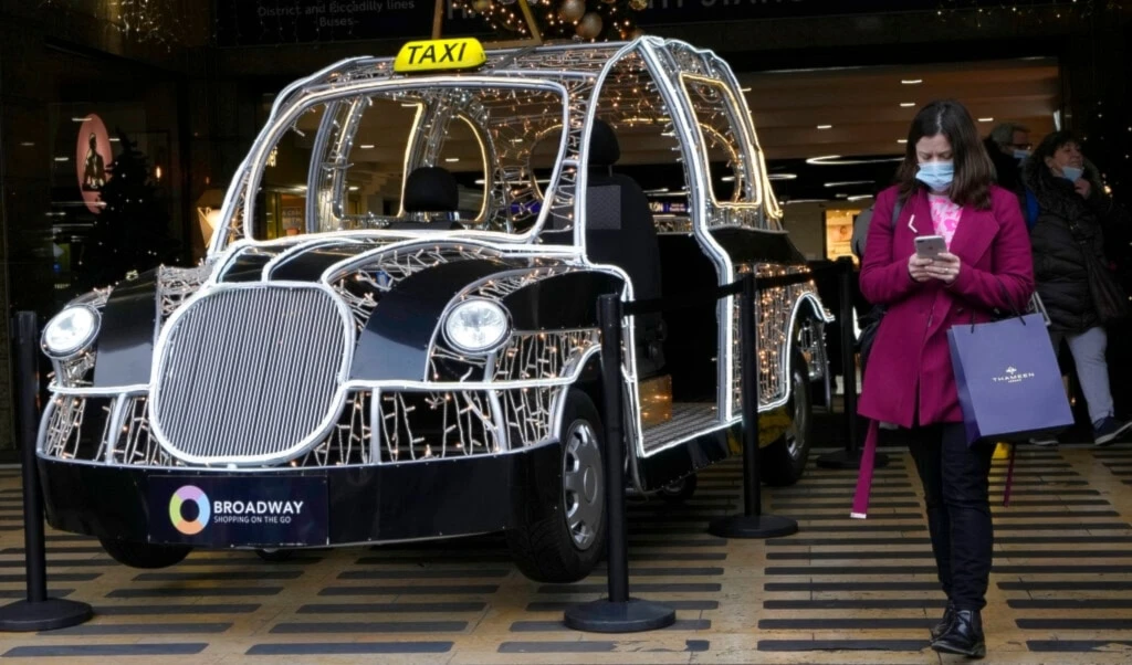 A shopper passes a seasonal decoration in the shape of a London taxi at the entrance to a shopping centre in London, Friday, Dec. 3, 2021. (AP)