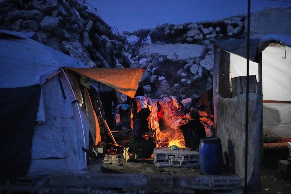 A displaced Palestinian woman and her son cook over an open fire beside their tent in Gaza City, Friday, November 28, 2025 (AP)