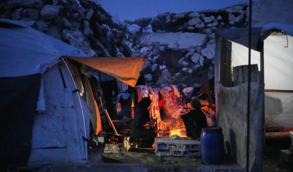 A displaced Palestinian woman and her son cook over an open fire beside their tent in Gaza City, Friday, November 28, 2025 (AP)