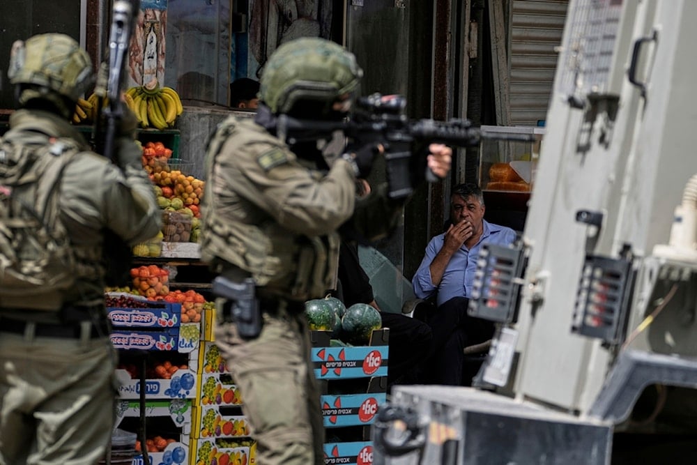 A Palestinian observes Israeli soldiers taking position on a street during a military raid in the West Bank city of Nablus, Tuesday, May 27, 2025. (AP Photo/Majdi Mohammed)
