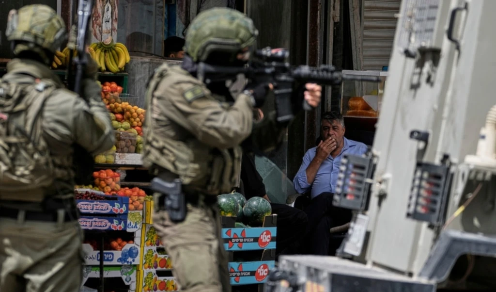 A Palestinian observes Israeli soldiers taking position on a street during a military raid in the West Bank city of Nablus, Tuesday, May 27, 2025. (AP Photo/Majdi Mohammed)