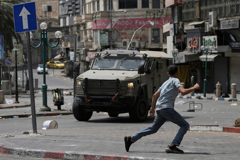 A Palestinian runs in front of an armored vehicle during clashes with Israeli forces following a military raid in the West Bank city of Nablus, Wednesday, Aug. 27, 2025 (AP)