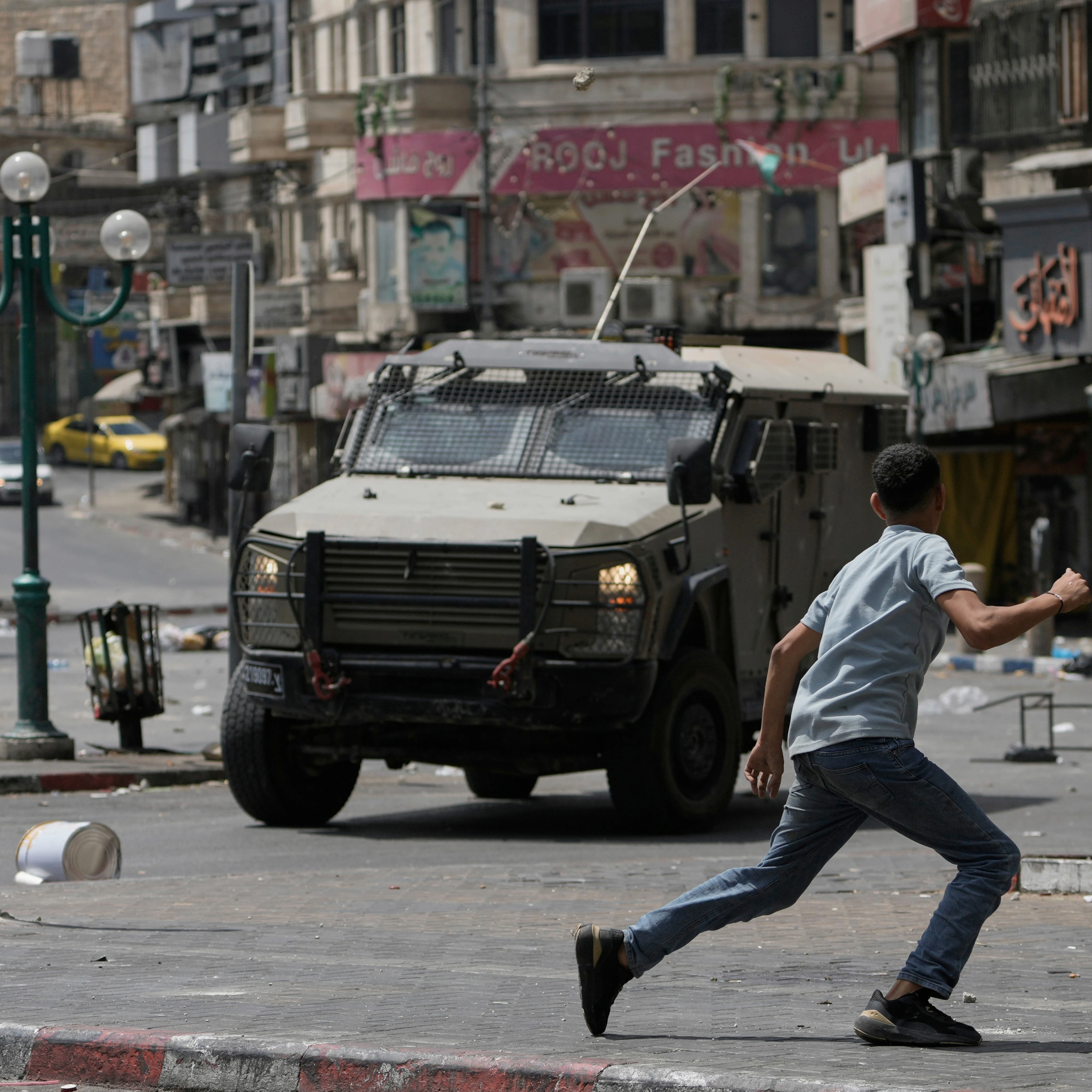 A Palestinian runs in front of an armored vehicle during clashes with Israeli forces following a military raid in the West Bank city of Nablus, Wednesday, Aug. 27, 2025 (AP)