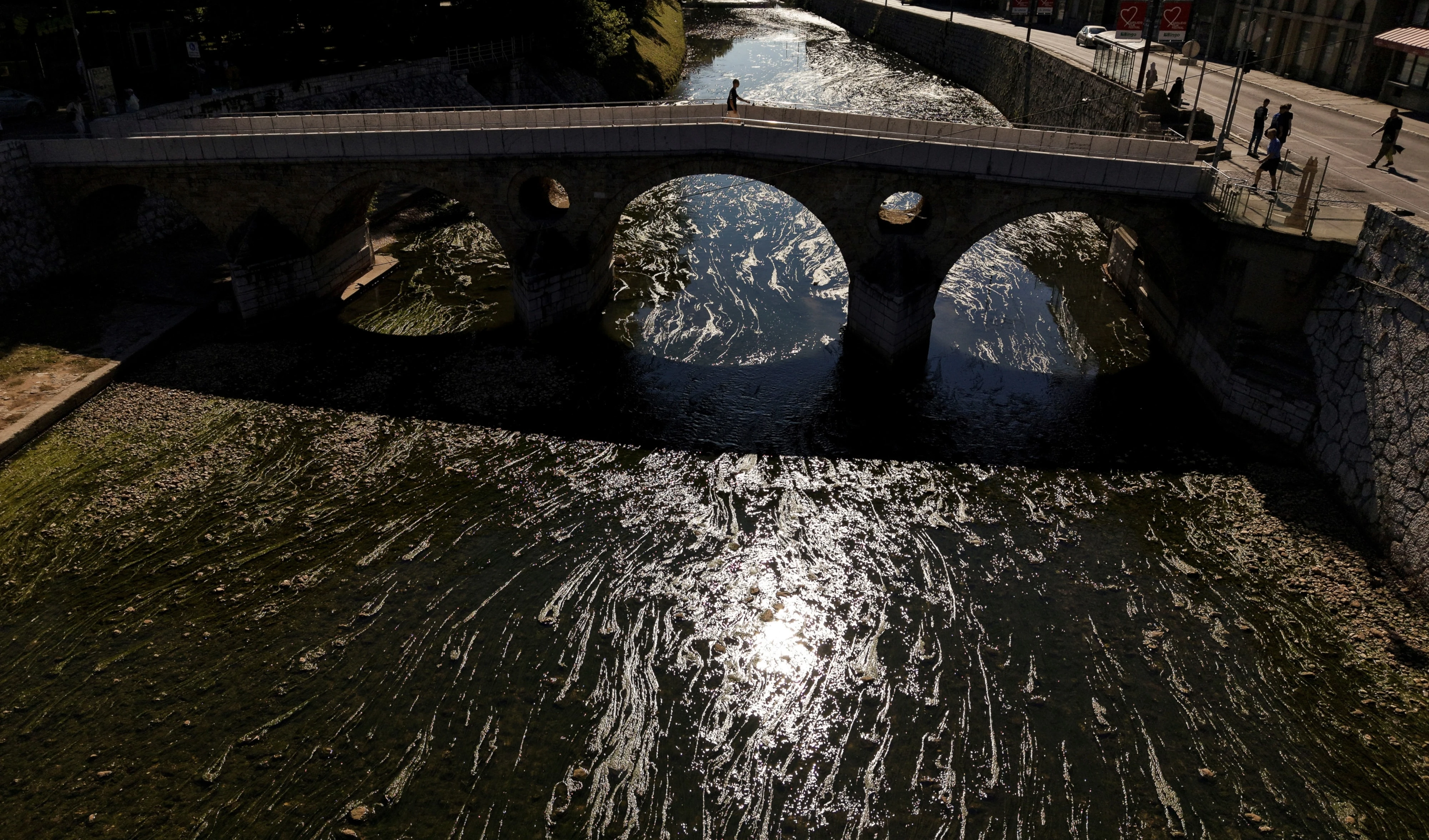 A person walks on a bridge over the Miljacka River, which is almost dried-up with algae visible, amid a heat wave and drought in Sarajevo, Bosnia, Sunday, Aug. 10, 2025 (AP)