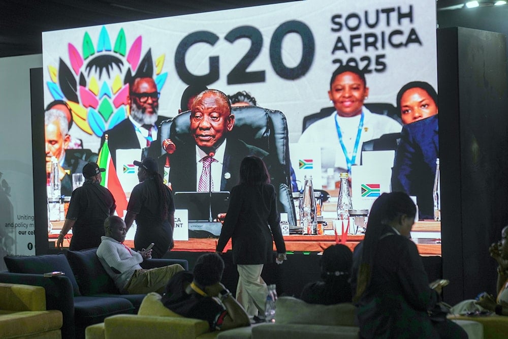 People walk by a large screen TV where South African President Cyril Ramaphosa holds a wooden gavel as he officially closes the G20 leaders' summit, in Johannesburg, South Africa, Sunday, Nov. 23, 2025 (AP)