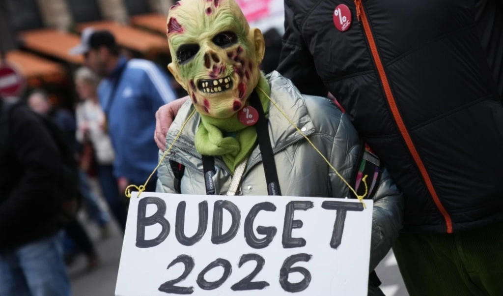 A protester holds a placard reading "Budget 2026" during a demonstration for higher wages and against austerity, in Paris, Tuesday, Dec. 2, 2025. (AP Photo/Christophe Ena)