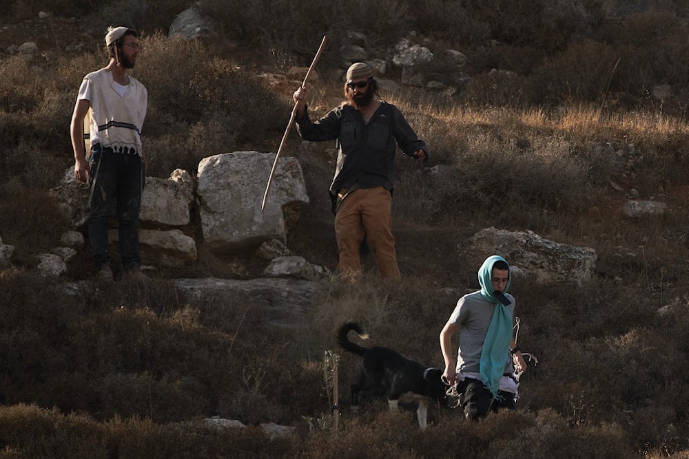 Israeli settlers walk down a hill as Israeli soldiers block access for Palestinians to an area for harvesting olives in the West Bank village of Sa'ir, near al-Khalil, Thursday, Oct. 23, 2025 (AP)