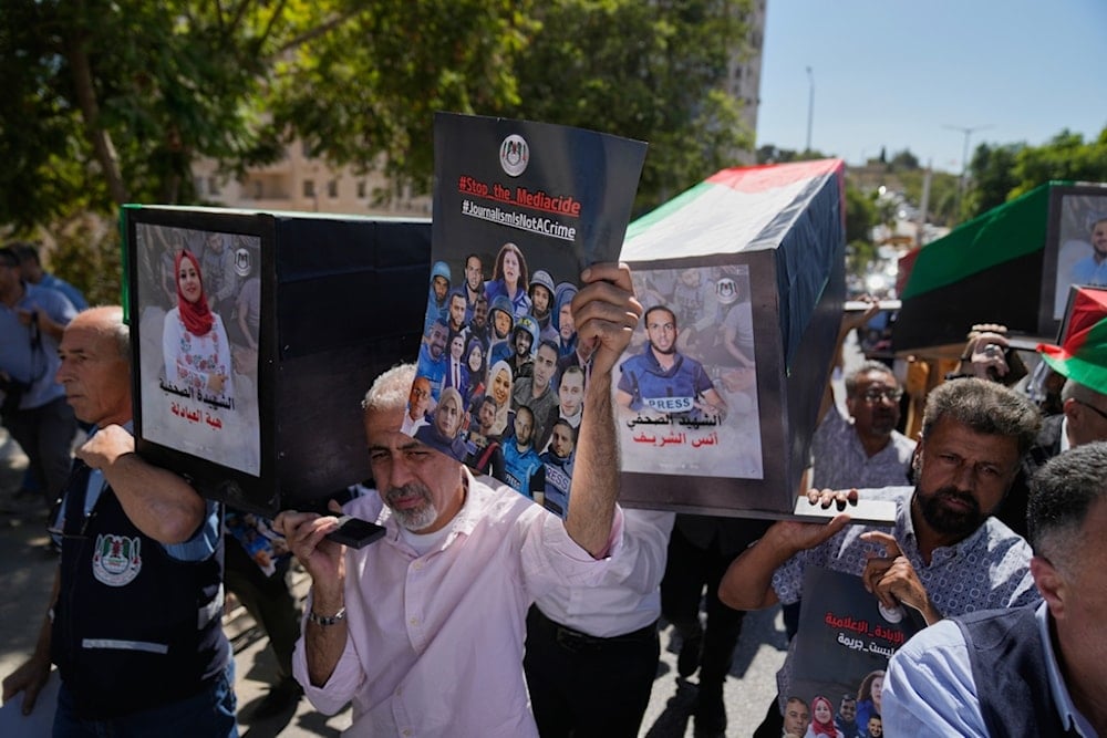 Palestinian journalists carry posters and mock coffins with pictures of their colleagues who were killed during the war on Gaza during a symbolic funeral in the West Bank city of Ramallah, Wednesday, October 8, 2025 (AP)