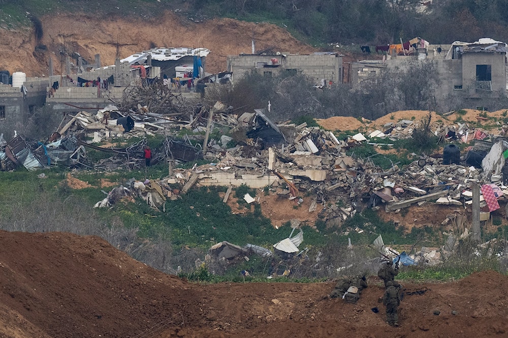 A Palestinian man wearing a red shirt, left, stands amid the rubble of destroyed buildings, watching Israeli soldiers, bottom right, take position in the northern Gaza Strip, as seen from southern “Israel”, Sunday, Feb. 9, 2025. (AP)