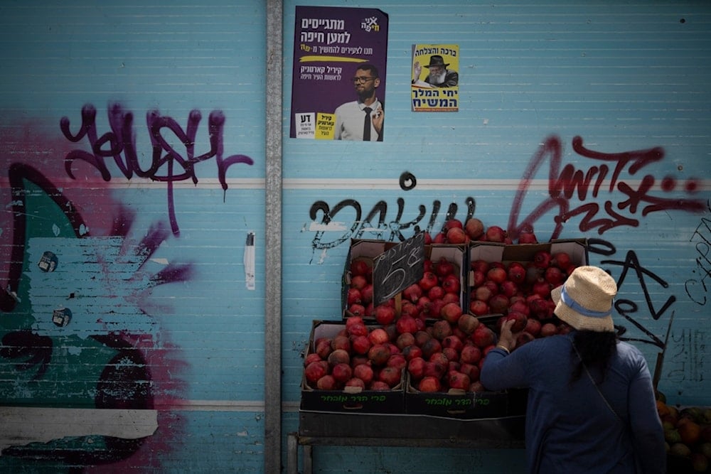 A woman checks the pomegranates displayed at a street market in Haifa, occupied Palestine, Friday, Aug. 16, 2024. (AP)